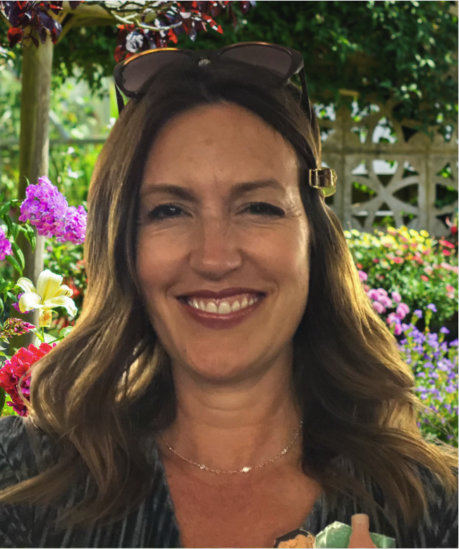 head shot of a smiling woman with brown hair and colorful flowers in the background